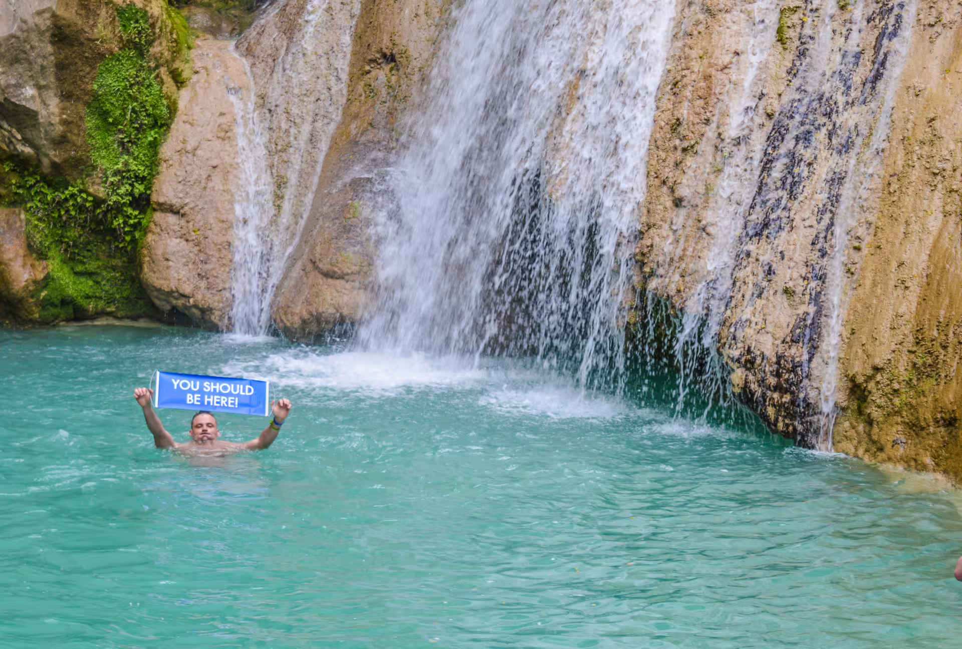 Swimmer in turquoise pool beneath Polylimnio Waterfalls, a top hiking and swimming tour near Kalamata