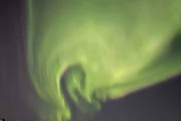Vibrant green northern lights swirling across a dark night sky during a professional photography tour