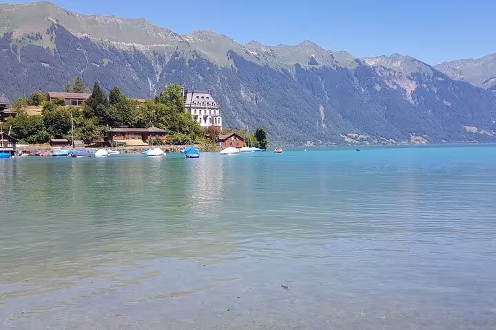 Idyllic lakeside scene in Swiss village with clear turquoise waters and mountain backdrop, perfect for serene Swiss tours.