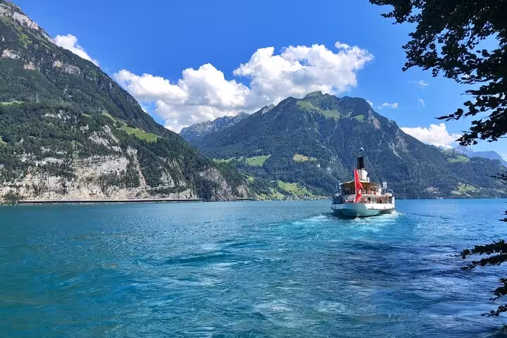 Scenic boat ride on a turquoise lake surrounded by lush Swiss Alps under a blue sky, ideal for nature tours.