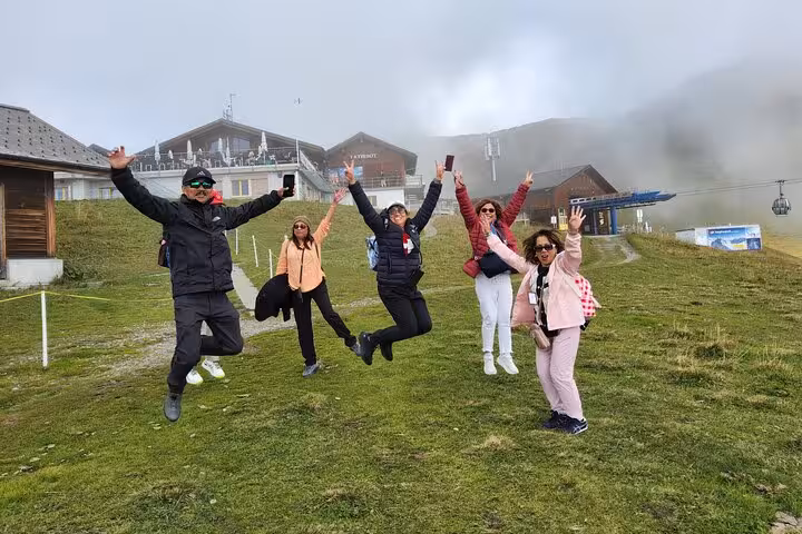 Happy travelers jumping on misty Swiss Alps meadow near cable car station, 4-day Zermatt Jungfrau tour