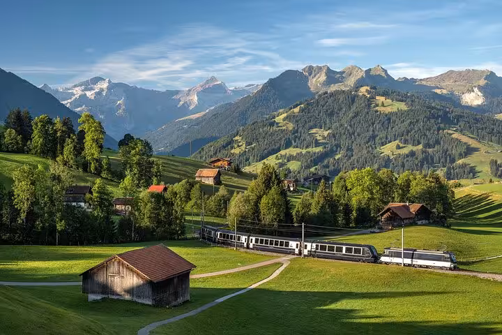 Train winds through picturesque Swiss valley with lush meadows and mountains, ideal for scenic rail journey.