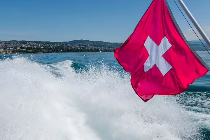 Swiss flag waves on a boat cruising Lake Zurich, highlighting the scenic beauty of the Zurich private tour.