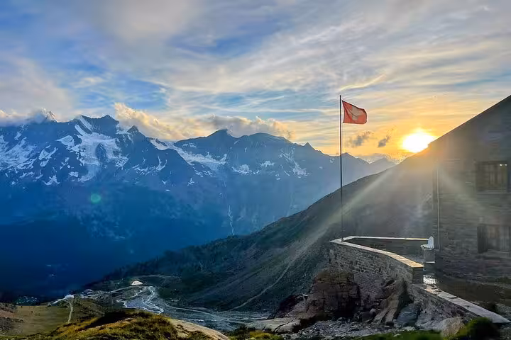 Swiss flag at mountain hut sunrise over alpine valley, scenic stop on 4-day Swiss Magic Alps trek