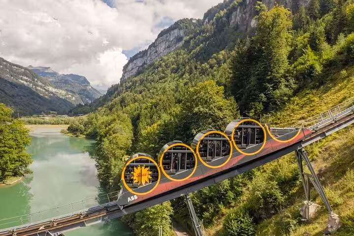 Scenic Swiss funicular train ascending lush hills, offering breathtaking views of mountains and a serene river below.