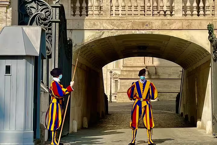Colorful Swiss Guards in traditional uniforms stand on duty at Vatican City gate, a highlight of Rome VIP Vatican tour