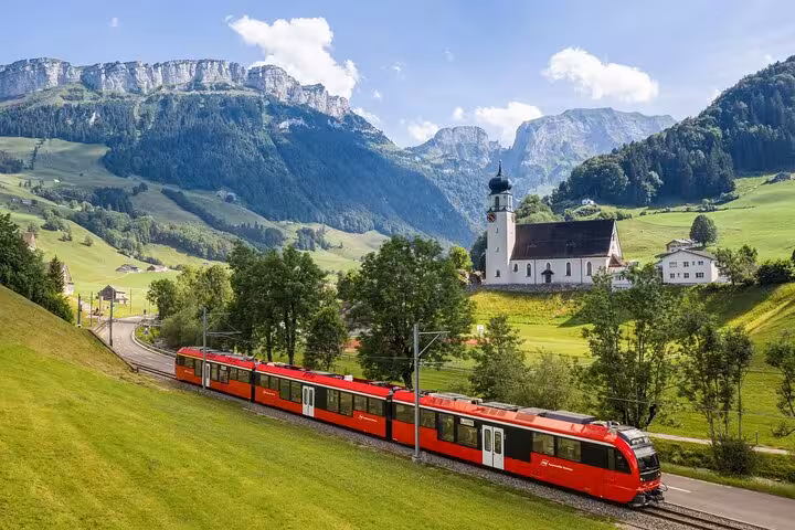 Scenic Swiss landscape with a red train passing through lush green hills and a picturesque church.