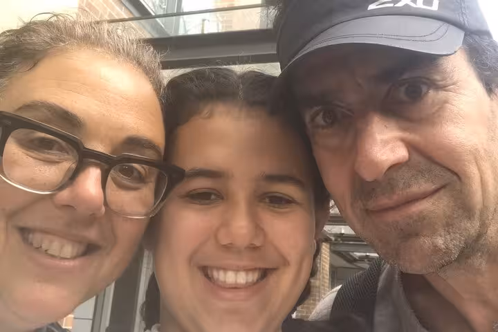Three smiling people posing together for a selfie outdoors near a brick building