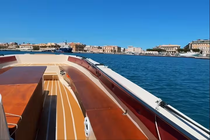 Elegant wooden private tour boat gliding through Syracuse harbor with Ortigia skyline and sea caves nearby