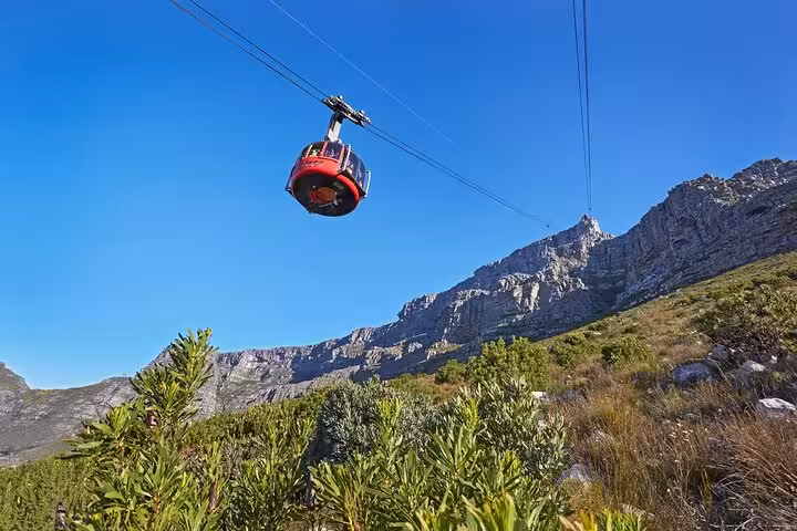 Red cable car ascending Table Mountain against a clear blue sky, offering breathtaking views and adventure.