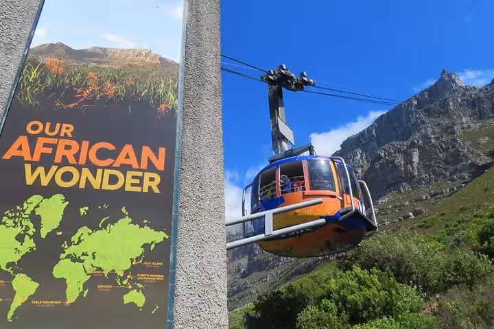 A colorful cable car ascends Table Mountain beside a sign highlighting the natural wonders of Cape Town.
