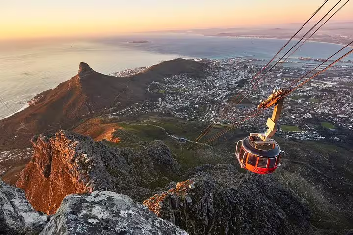 Aerial view of a cable car ascending Table Mountain at sunset, overlooking Cape Town and the Atlantic Ocean.