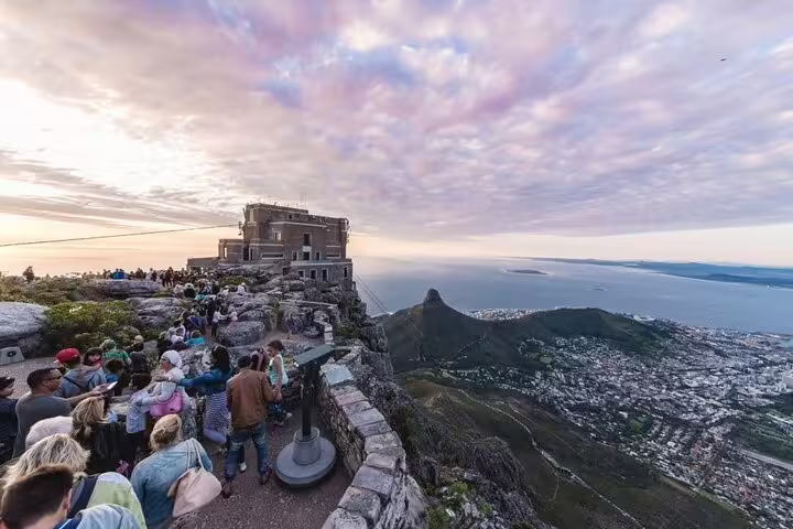 Tourists enjoy breathtaking views from Table Mountain summit, overlooking Cape Town and Atlantic Ocean at sunset.