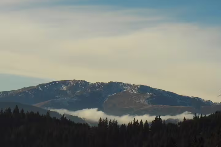 Snow-dusted Taga Mountains peak with low clouds drifting through forested valleys near Brasov