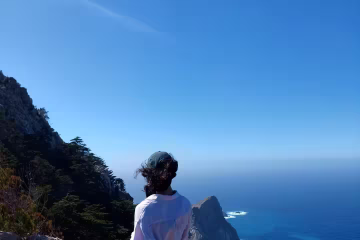 A hiker enjoys a stunning ocean view from a rocky cliff, embodying the freedom and customization of our tailored hiking tours.