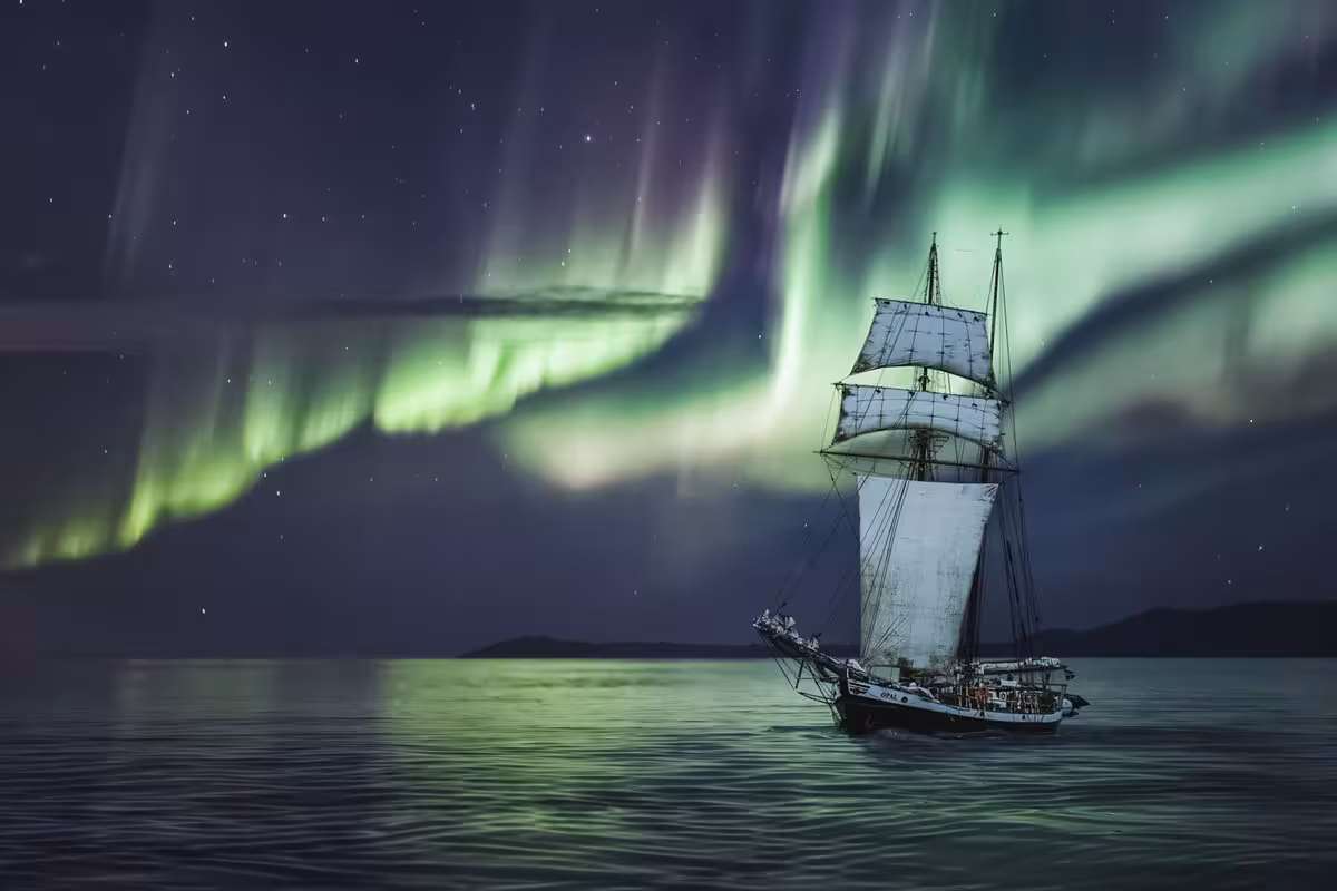 Majestic tall ship sailing under breathtaking Northern Lights aurora borealis on a premium Arctic luxury cruise night voyage.