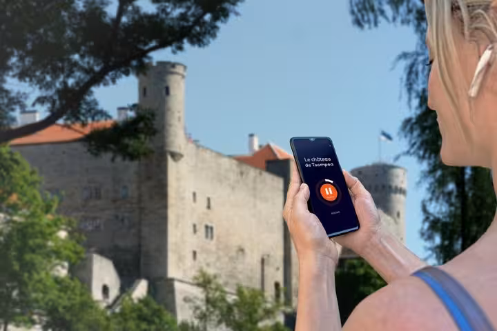 Tourist using audio guide app on smartphone with Toompea Castle in background, Tallinn