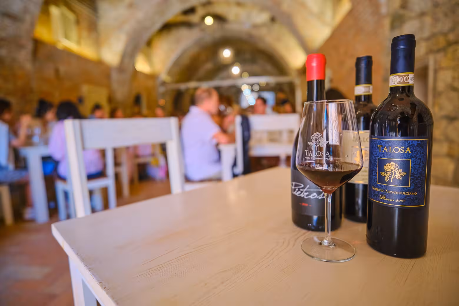 Close-up of Talosa wine bottles and glass in a rustic Val D'Orcia setting, ideal for a Montepulciano and Pienza wine tour.
