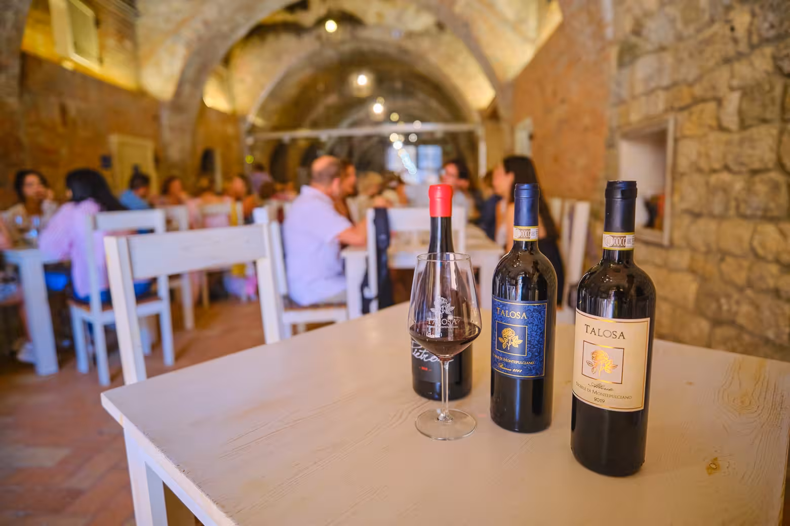 Bottles of Talosa wine and a glass on a table in a charming Val D'Orcia cellar, perfect for wine tasting tours in Tuscany.