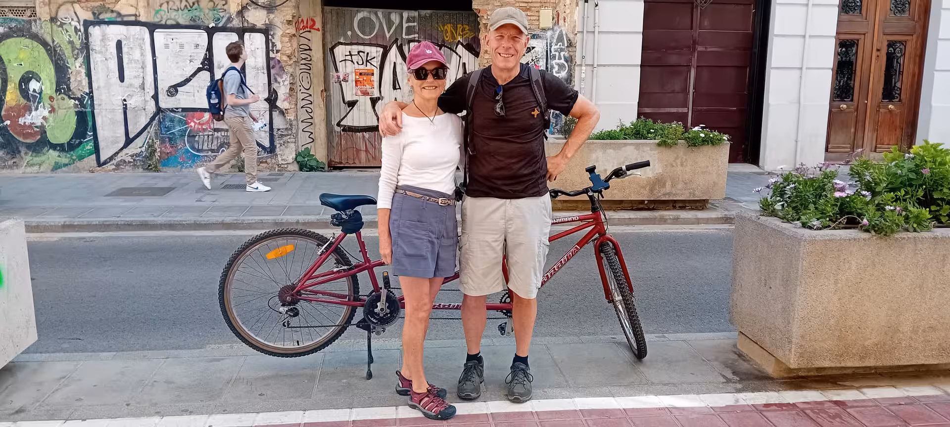 Happy couple posing with a red tandem bike on a Valencia city street during a half-day or full-day bike rental tour.