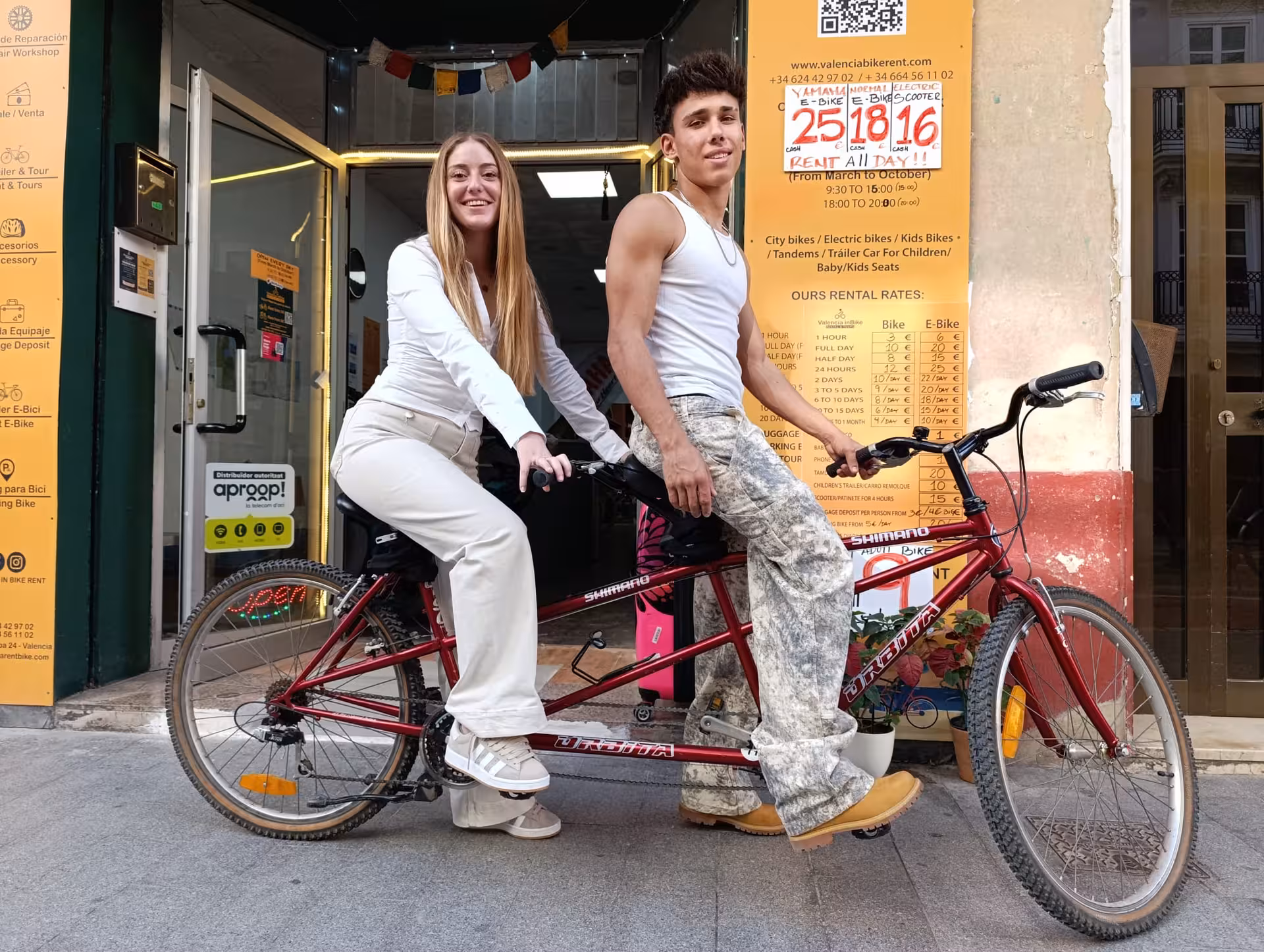 Two happy riders posing on a red tandem bike outside Valencia Bike Rent shop for a half or full day rental