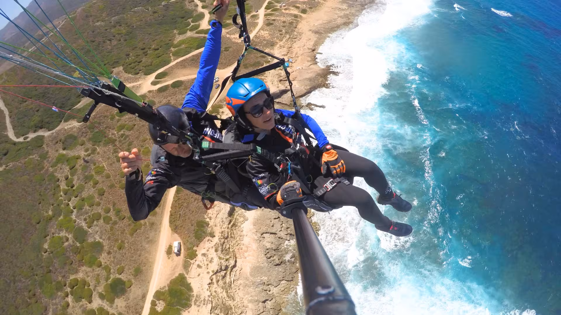Tandem paragliding flight over Littigheddu coastline with stunning aerial view of the turquoise sea and cliffs.