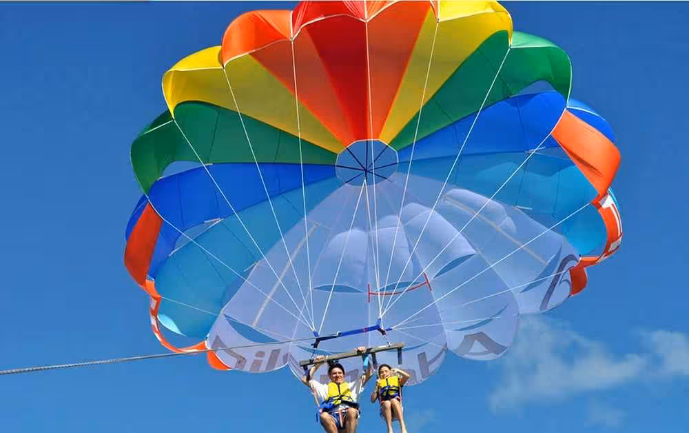 Tandem parasailing trip with two riders under a rainbow canopy, soaring high in a clear blue sky