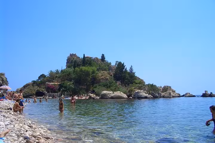Relaxing beach scene in Taormina with clear waters and a lush, green island under a bright blue sky.