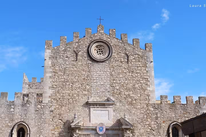 Historic stone facade of Taormina Cathedral under a bright blue sky, showcasing its medieval architectural beauty.