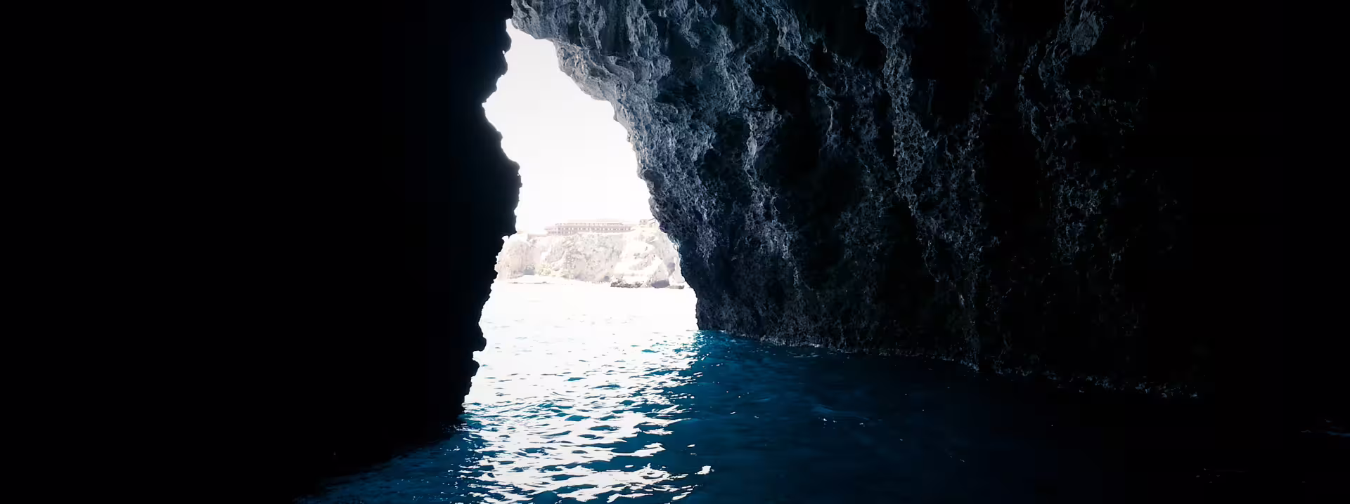 Entering a sea cave on a private Taormina boat tour, dark volcanic rock and shimmering Ionian waters