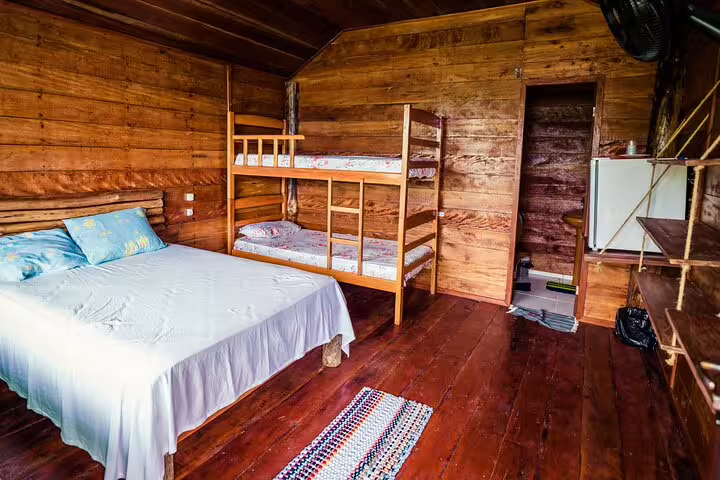 Cozy wooden cabin interior with double bed and bunk bed at Tapiri Rio Negro Lodge in the jungle.