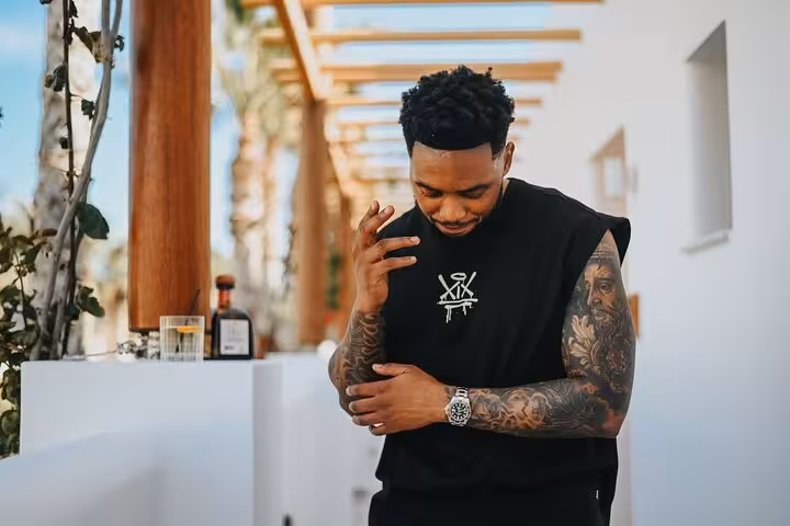 Man with tattoos poses stylishly in a modern outdoor setting in Malia, showcasing a unique photoshoot experience.