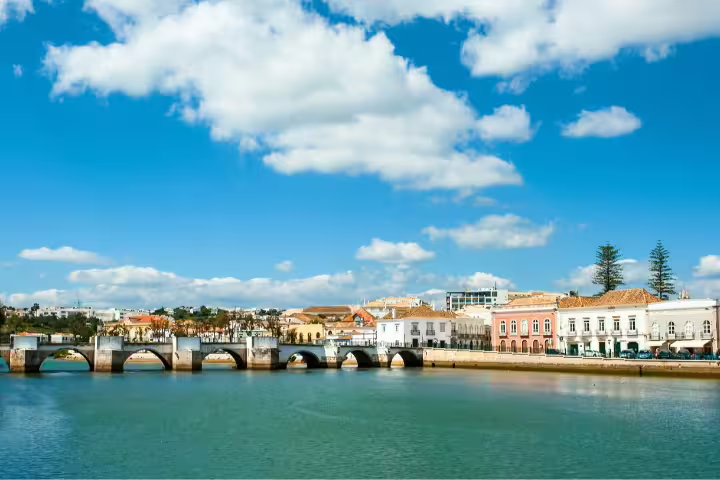 Picturesque view of Tavira's Roman bridge and colorful buildings under a vibrant blue sky, Algarve, Portugal self-drive tour.
