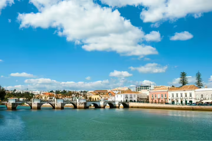 Scenic view of Tavira's Roman bridge and historic waterfront under a blue sky, featured in Discovering Algarve self-drive tour.