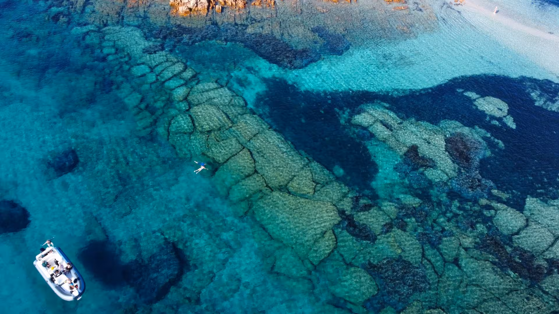 Aerial view of Tavolara Island's crystal-clear waters with snorkelers and dinghy tour, perfect for Olbia excursions.