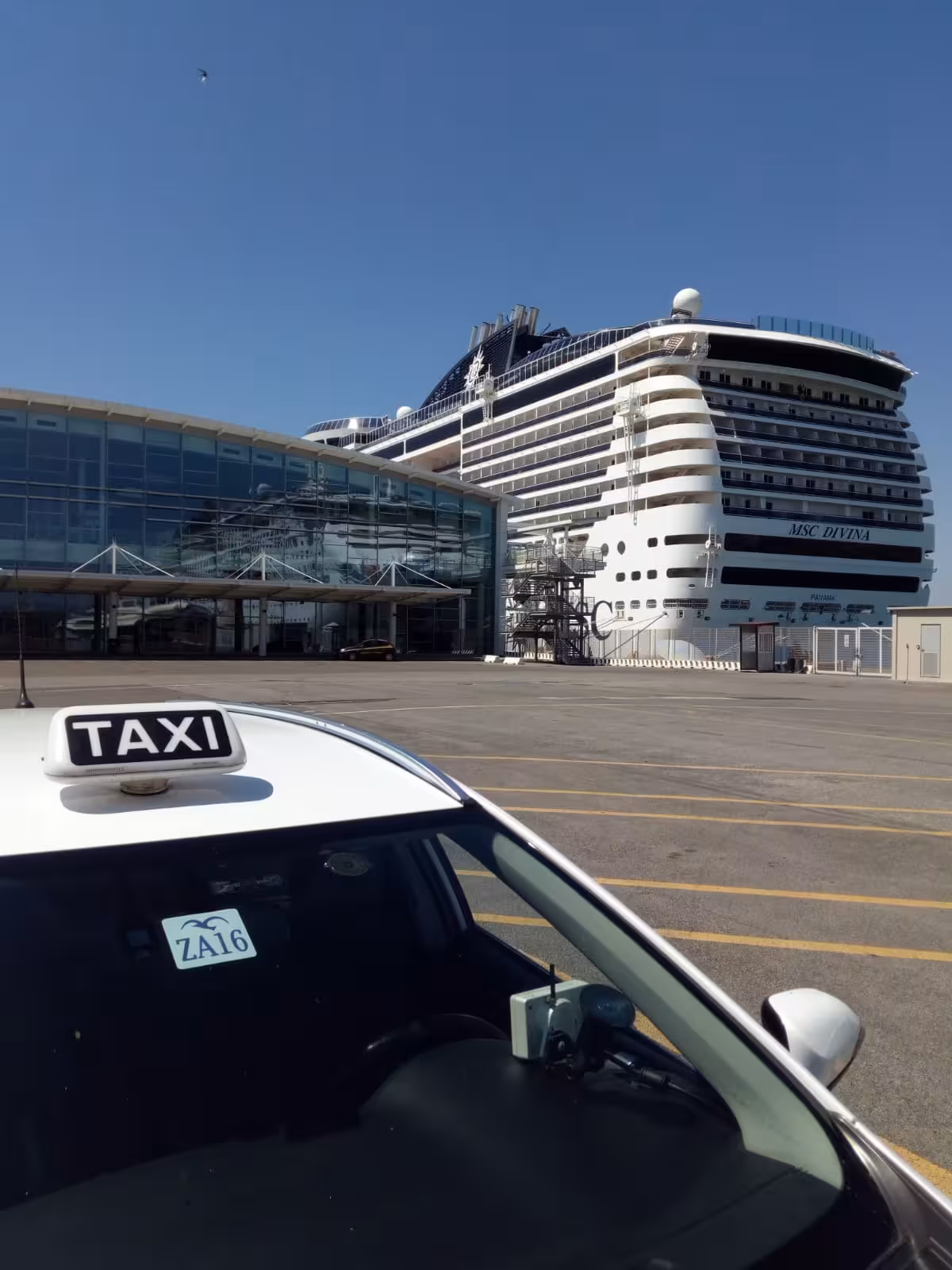 Taxi waiting outside the Civitavecchia cruise terminal with MSC Divina docked, ready for transfer to Fiumicino airport.