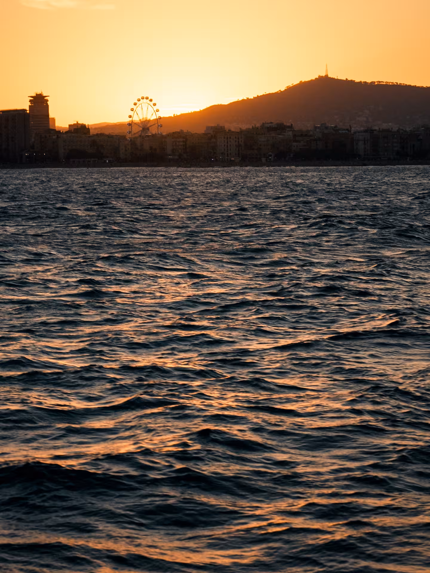 Golden sunset over the sea with city skyline silhouette, a serene backdrop for a relaxing tea ceremony cruise