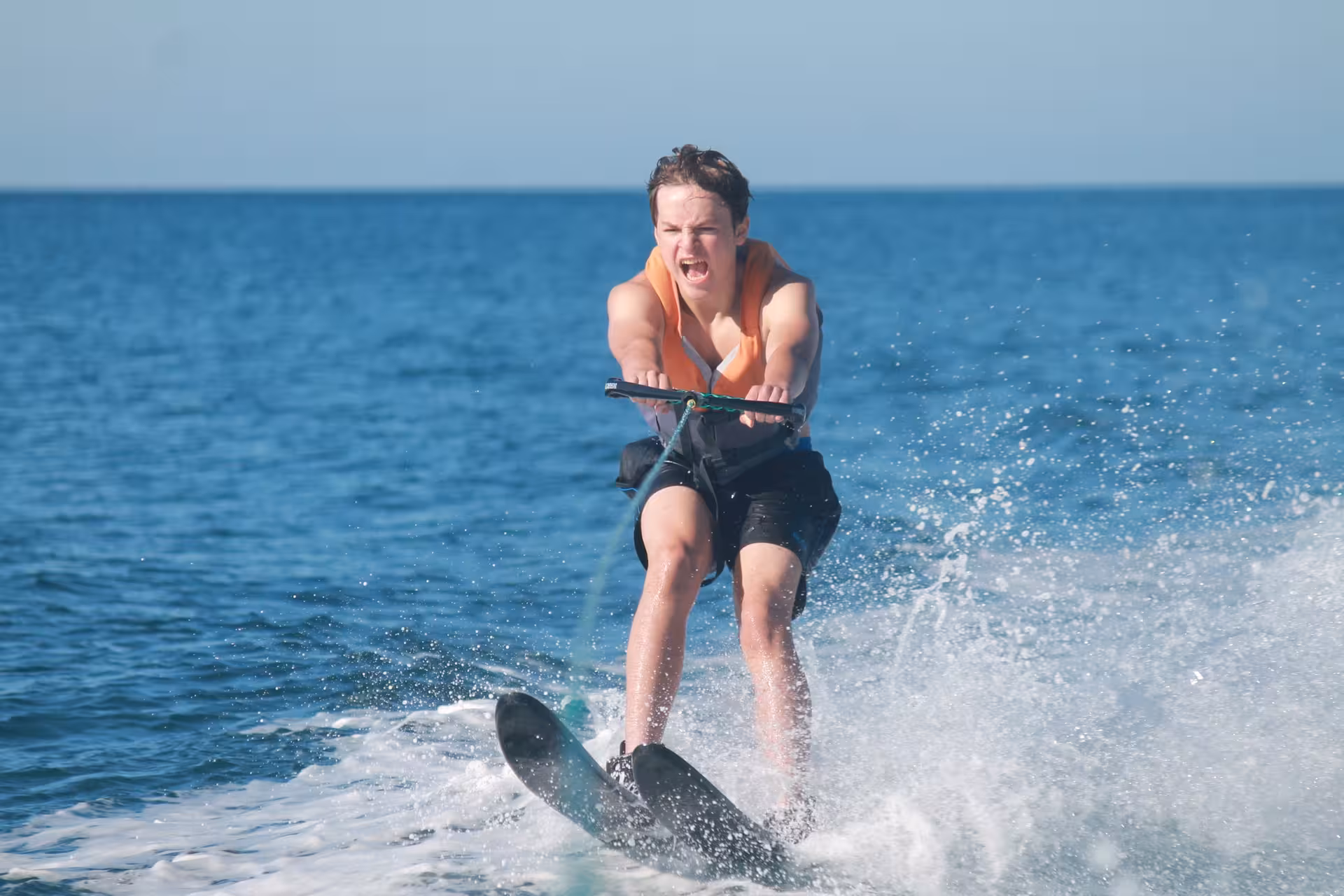 Energetic teen water skiing in Armacao de Pera Algarve wearing life jacket speeding across sparkling ocean waves
