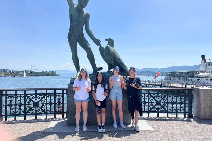 Teens posing at Ganymede statue on Lake Zurich promenade during a Zurich scavenger hunt and sights tour