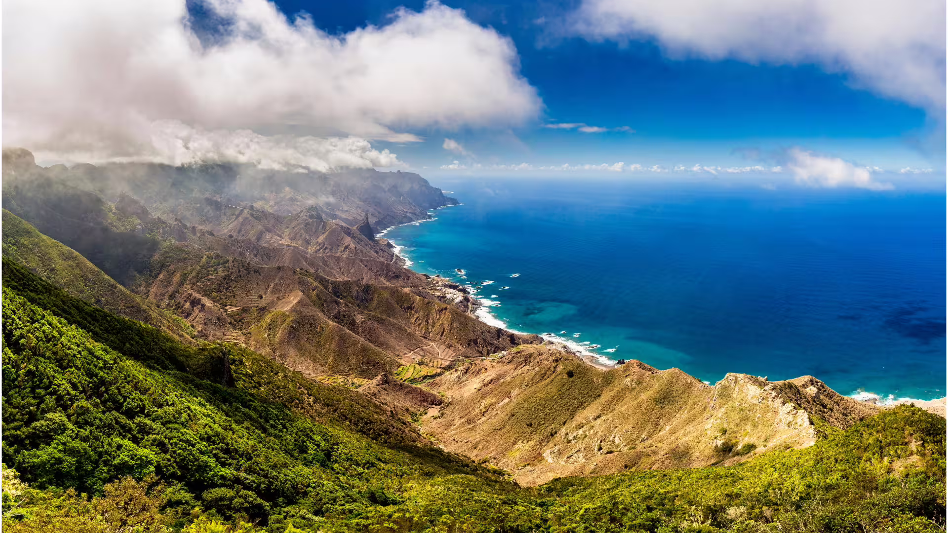 Breathtaking aerial view of lush green hills meeting the azure coastline, enveloped in misty clouds.