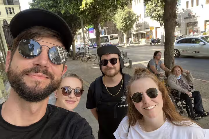 Group of four friends taking a selfie on a sunny Tel Aviv street during a walking tour