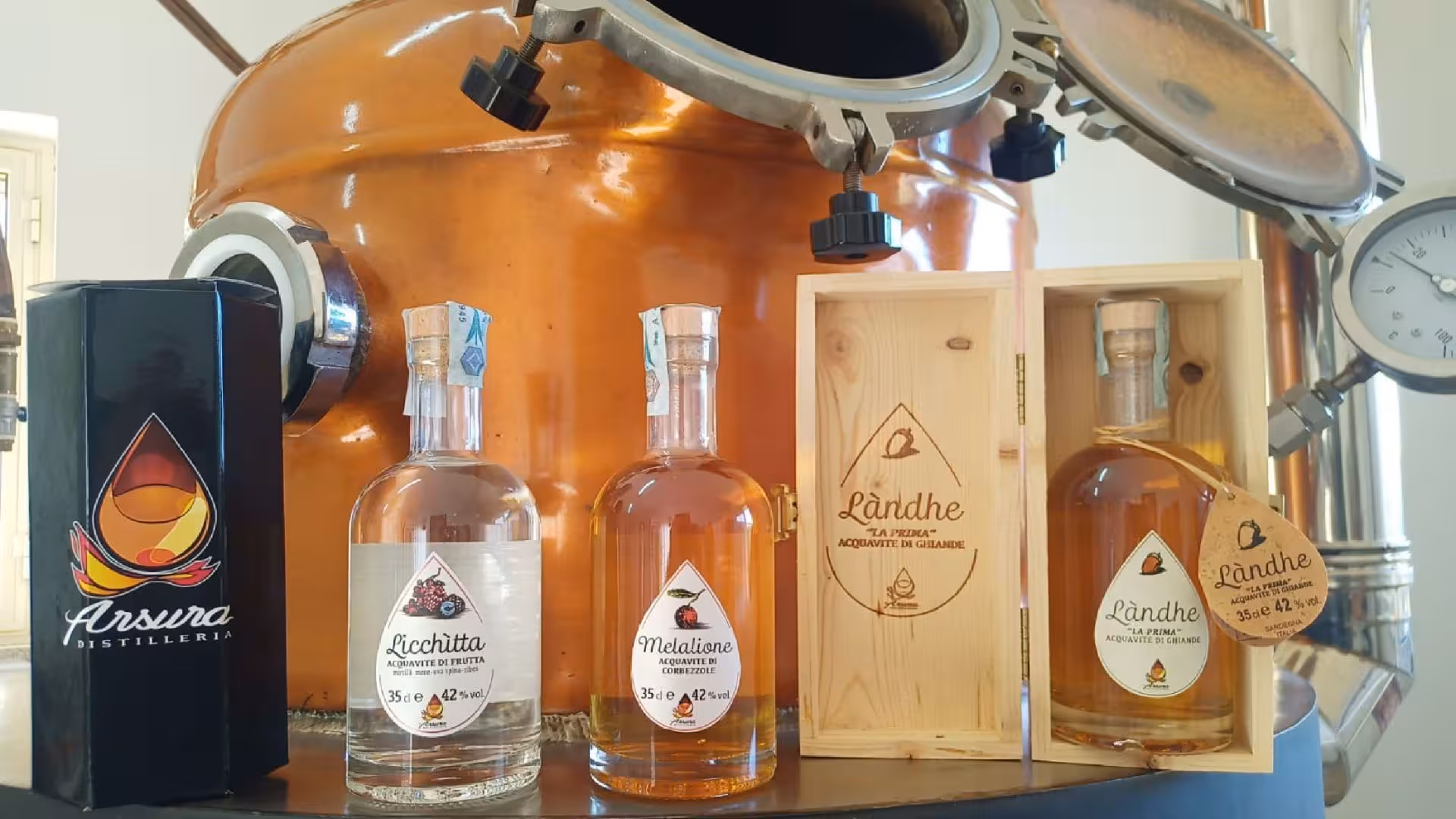 Display of artisanal distillates bottles next to copper still at Tempio Pausania workshop tour.