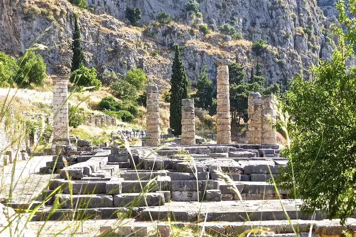 Ruins of the Temple of Apollo in Delphi surrounded by lush greenery and rugged mountains.
