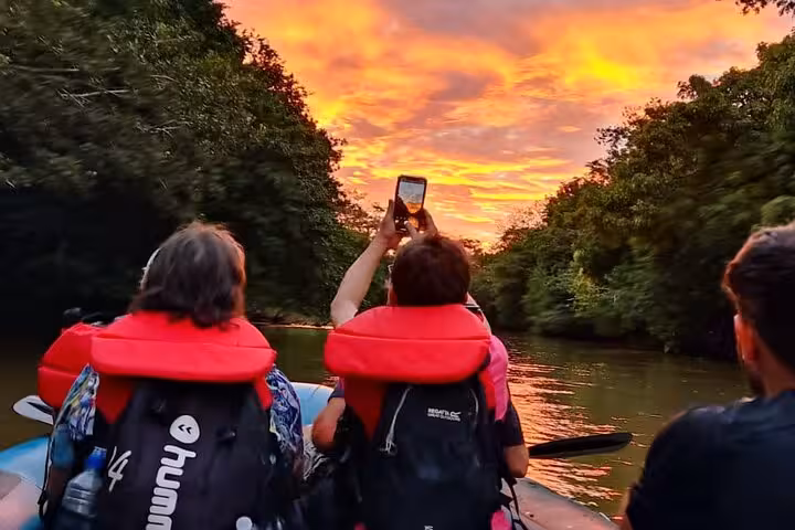 Tourists capturing a stunning sunset during a Tenorio wildlife safari boat tour, highlighting bird watching opportunities.