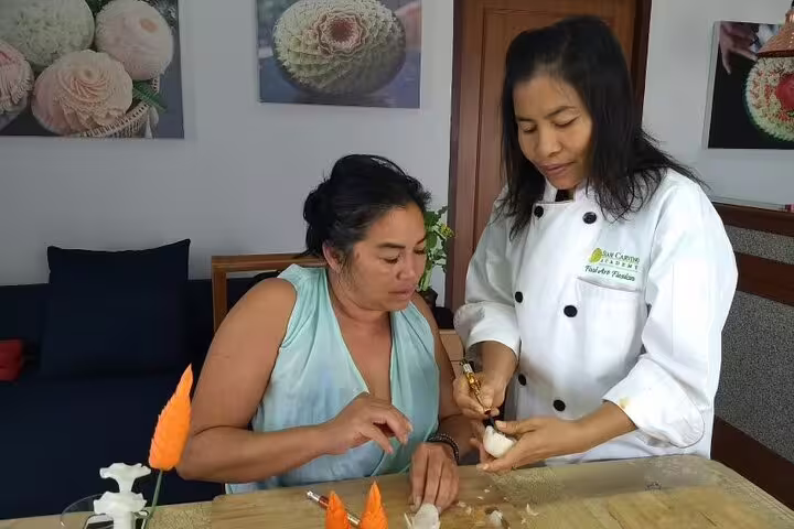 Thai chef instructor guiding a student in hands-on fruit carving during a professional half-day class in Thailand