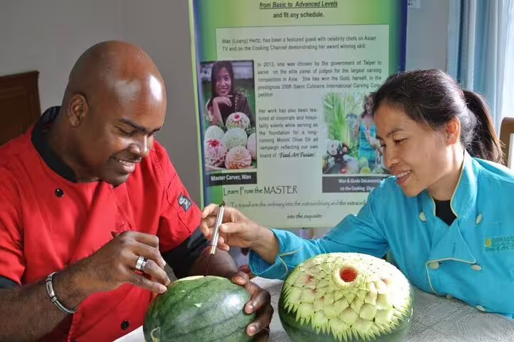 Expert Thai carving instructor guides student in intricate watermelon fruit carving during a professional half-day class