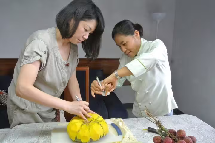Thai chef assists student in carving a yellow pumpkin during a professional fruit and vegetable carving class