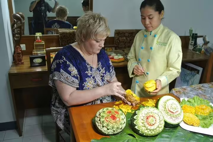 Thai chef instructor guides a tourist in hands-on fruit and vegetable carving class with intricate melon designs