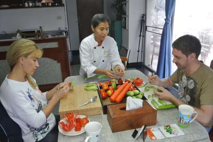 Expert Thai chef teaching two students vegetable carving techniques with fresh produce in a half-day carving class