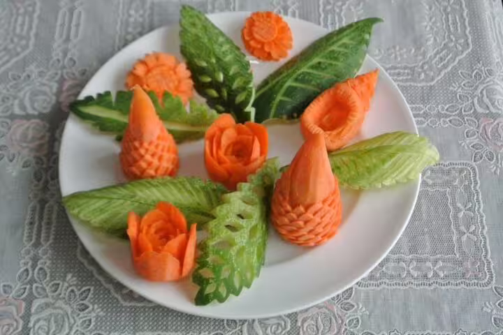 Elegant Thai vegetable carving display with carved carrots and cucumbers shaped into flowers on a white plate